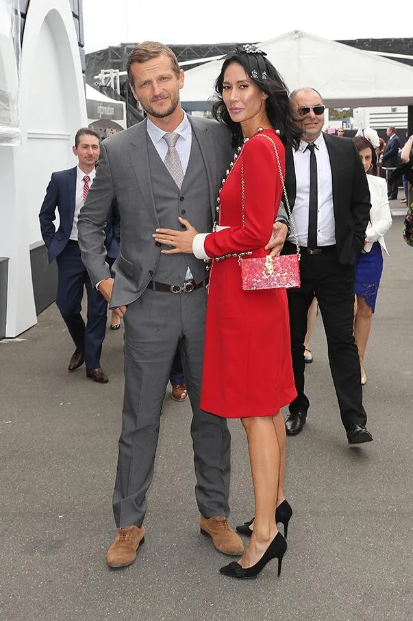 Man in a grey suit and woman in a red dress posing together at an outdoor event.