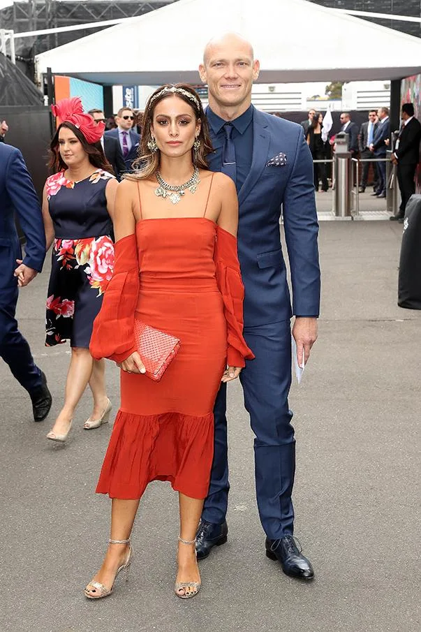 Couple posing at an outdoor event; woman in red dress, man in blue suit.