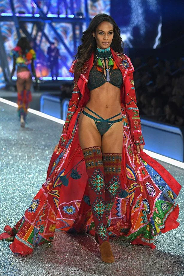 Model walking on a glittery runway wearing colorful lingerie and a flowing red robe with intricate patterns.