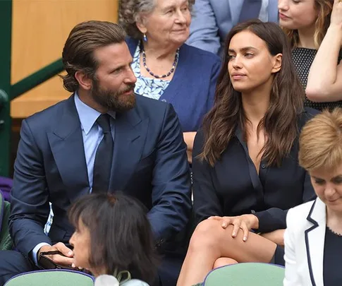 A man in a blue suit and a woman in a black outfit sit together in a crowded event.