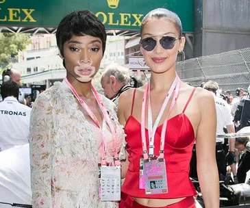 Two women dressed stylishly with event passes, pose at the Monaco Grand Prix, surrounded by event staff.