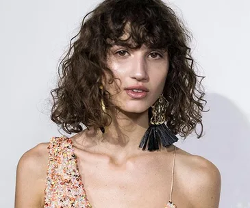 Model with curly bob hairstyle wearing asymmetrical sequin dress and statement earrings at MBFWA 2017.