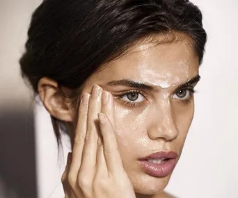 Woman applying hyaluronic acid serum to her face, focusing on her cheeks and forehead.