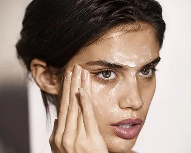 Woman applying hyaluronic acid serum to her face, focusing on her cheeks and forehead.