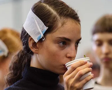 Young woman drinking from a white cup with hair clips in her hair.