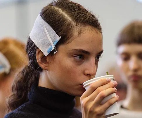 Young woman drinking from a white cup with hair clips in her hair.