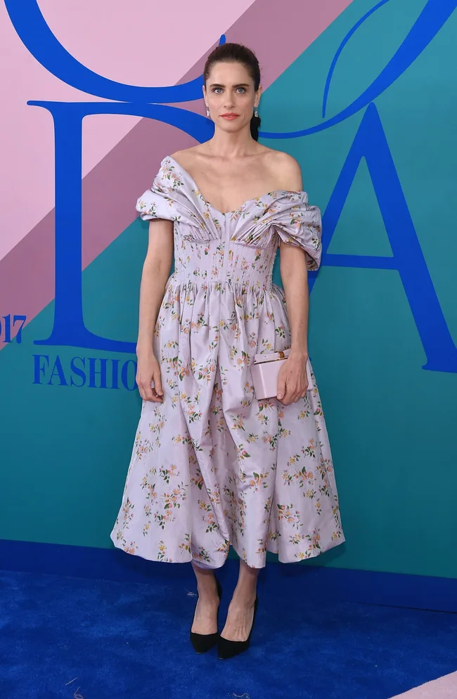 Woman in floral off-shoulder dress on blue carpet at fashion event.