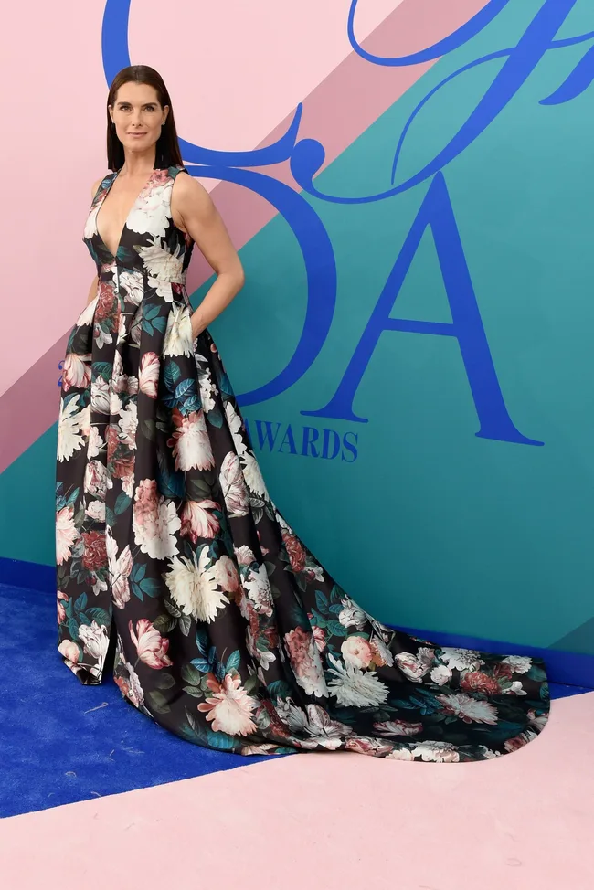 Woman in a floral gown poses in front of a colorful backdrop at an awards event.