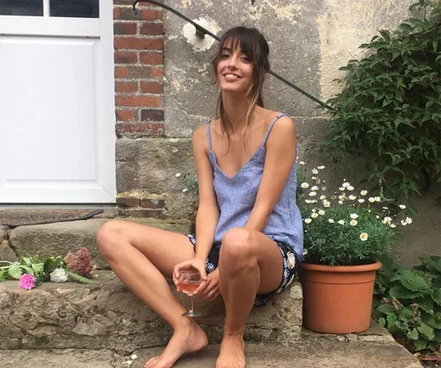 A woman sitting on stone steps, holding a glass of rosato wine, smiling with flowers and plants around.