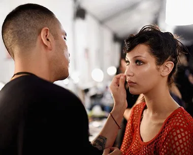 Makeup artist applying makeup to a model's face backstage.