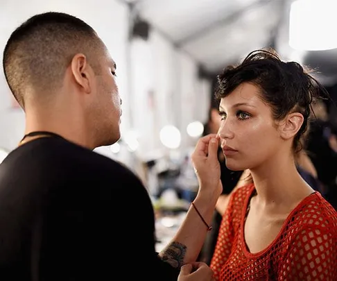 Makeup artist applying makeup to a model's face backstage.