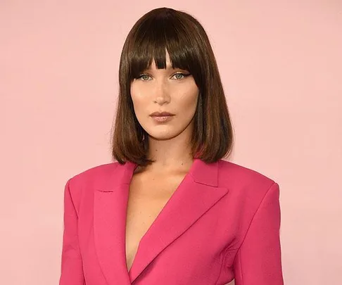 Woman with shoulder-length brown hair and bangs wearing a bright pink blazer against a pink background.