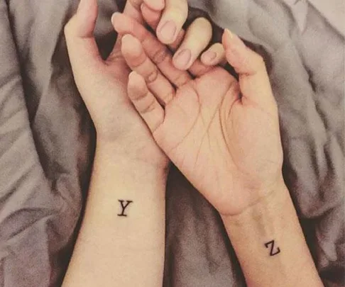 Close-up of two wrists showing temporary tattoos of the letters "Y" and "Z" on a soft fabric background.