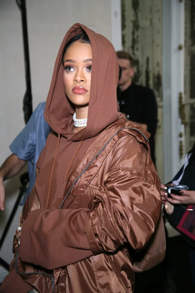 A person in a brown hooded outfit with pearl necklace at an event.