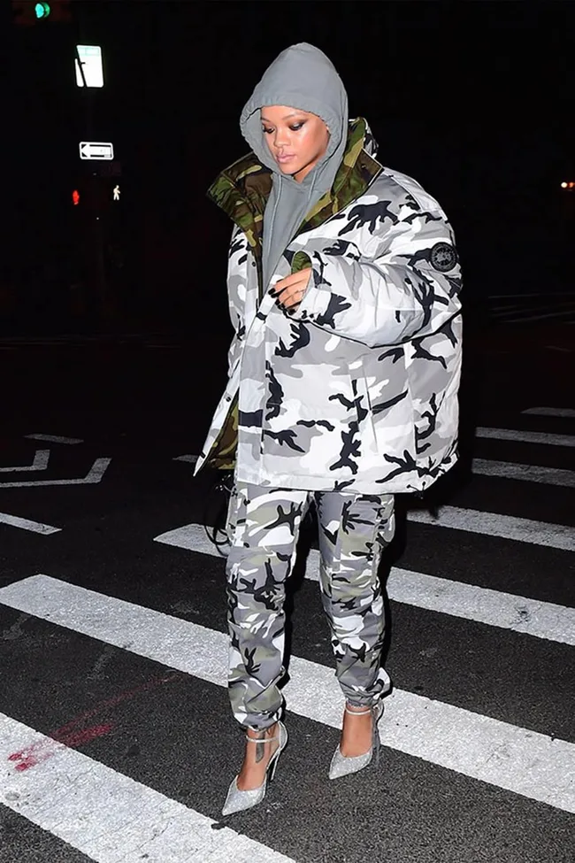 Person in camo outfit and heels walking on a city street at night.