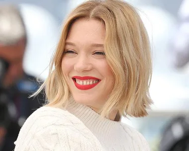 Woman with a blonde bob hairstyle smiling, wearing a white sweater.