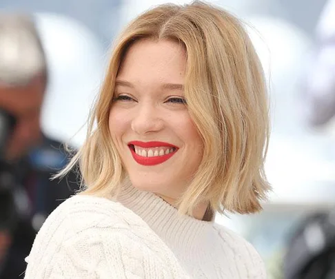 Woman with a blonde bob hairstyle smiling, wearing a white sweater.