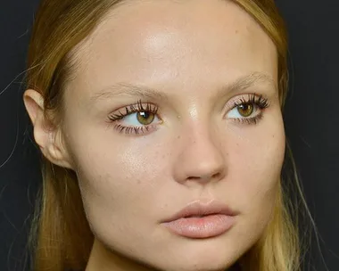 Close-up of a model with natural makeup and defined lashes against a dark background.