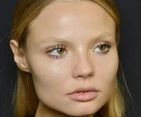 Close-up of a model with natural makeup and defined lashes against a dark background.