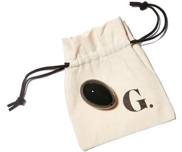 A jade yoni egg on a drawstring pouch with the letter "G." printed on it.