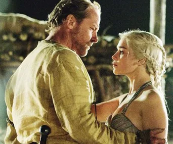 Jorah Mormont and Daenerys Targaryen stand close, looking at each other intently, in a scene from Game of Thrones.