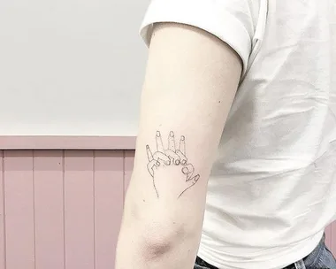 A line drawing of two hands holding each other tattooed on the inside of an upper arm.