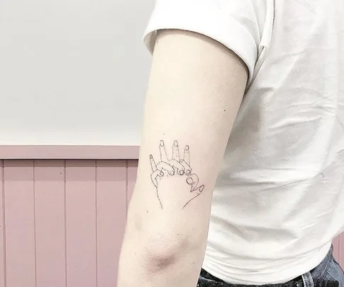 A line drawing of two hands holding each other tattooed on the inside of an upper arm.