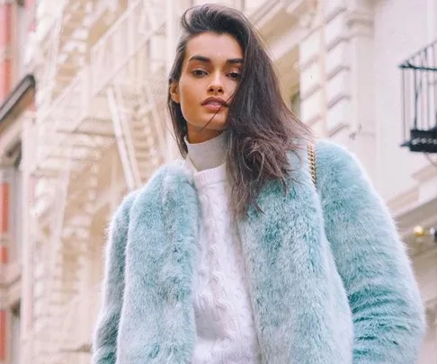 Model wearing a light blue fur coat over a white sweater on an urban street.