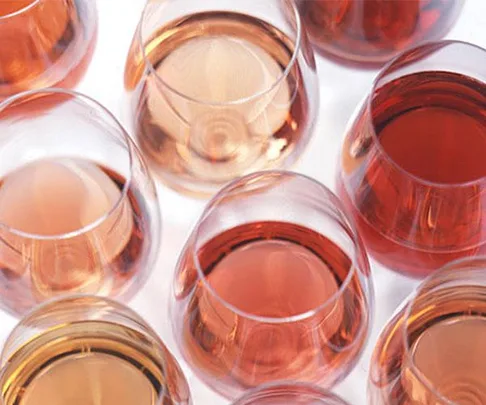 A variety of pink-hued spirits in glasses seen from above on a white background.