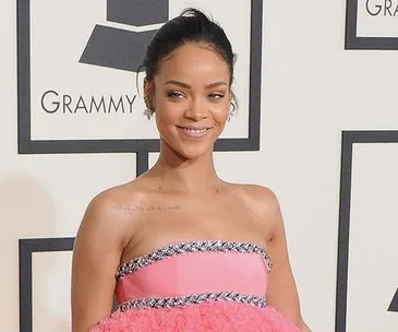 Rihanna at the Grammy Awards in a pink strapless gown, standing in front of a backdrop with the Grammy logo.