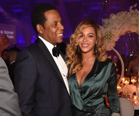 A couple dressed elegantly smiling at an event, with floral decorations and candles in the background.