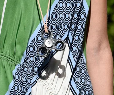 A model wearing a green and patterned dress features a fidget spinner necklace at New York Fashion Week.