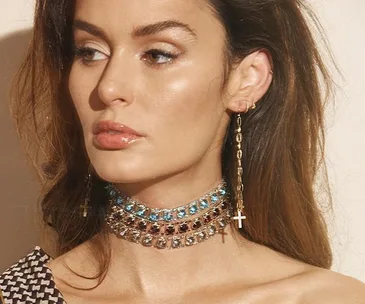 Woman wearing layered jeweled choker and cross earrings, looking to the side.