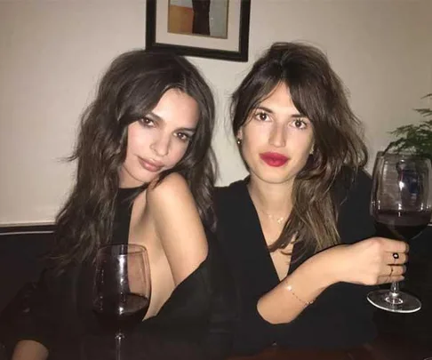 Two women sitting together at a table, each holding a glass of red wine, with one woman leaning her head on her hand.