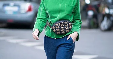 Person wearing a green top, blue pants, and a stylish Gucci fanny pack with gold embellishments on a city street.