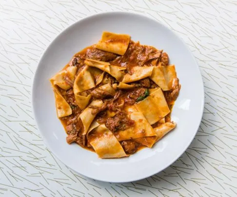 A plate of pappardelle pasta with rich meat ragu sauce served on a white plate.