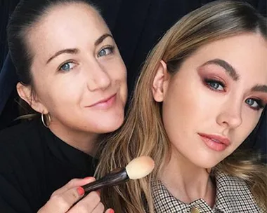 Makeup artist applying finishing touches with a brush on a model with glamorous makeup.