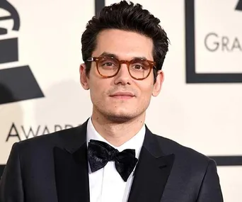 Man with dark hair and glasses wearing a black tuxedo, standing at an award event.