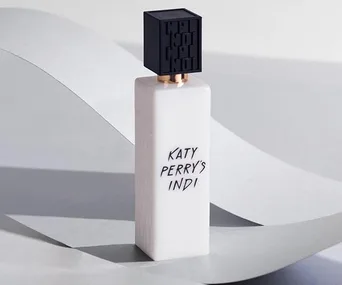 Katy Perry’s Indi perfume bottle with a black cap on a light grey background.