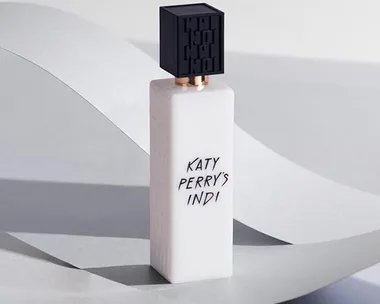 Katy Perry’s Indi perfume bottle with a black cap on a light grey background.