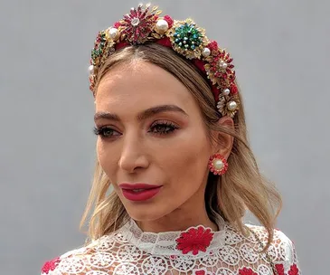 A woman wearing a colorful jeweled headpiece and lace dress with floral embroidery at the Melbourne Cup.