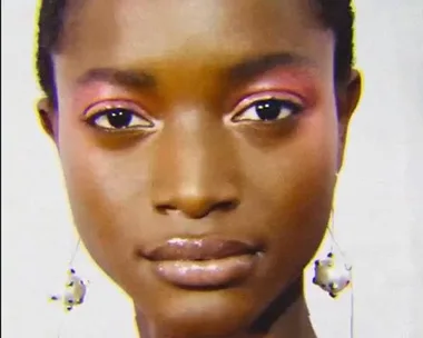 Close-up of a model with radiant skin, glossy lips, pink eyeshadow, and dangling earrings.