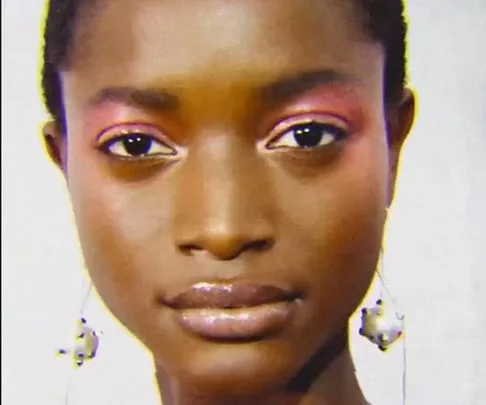 Close-up of a model with radiant skin, glossy lips, pink eyeshadow, and dangling earrings.