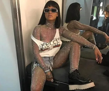 Person wearing sparkling mesh bodysuit, Gucci tank top, shorts, platform shoes, and sunglasses, posing casually.