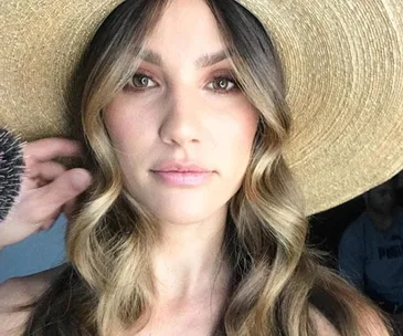 Woman with wavy hair wearing a large hat, being prepared for Melbourne Cup 2017.