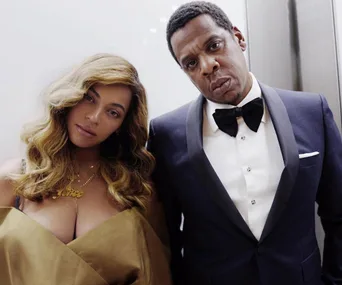 Beyoncé and Jay-Z posing together, Beyoncé with wavy hair and an off-shoulder outfit, Jay-Z in a tuxedo with a bow tie.