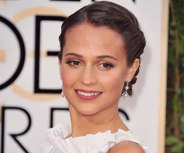 A person with a braided updo and diamond earrings, smiling at an event.