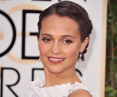 A person with a braided updo and diamond earrings, smiling at an event.