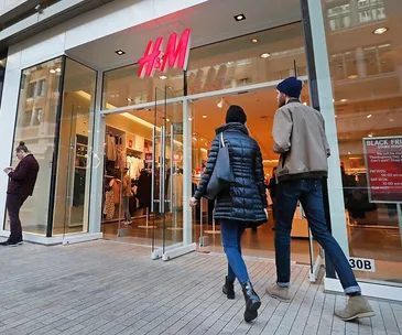 Two people entering an H&M store with a large red and white H&M logo above the entrance.