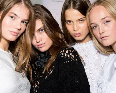 Four models with different hairstyles and colors, posing together at a fashion show, wearing various white and black outfits.